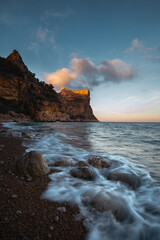 The rock rises above the blue sea at sunset or sunrise