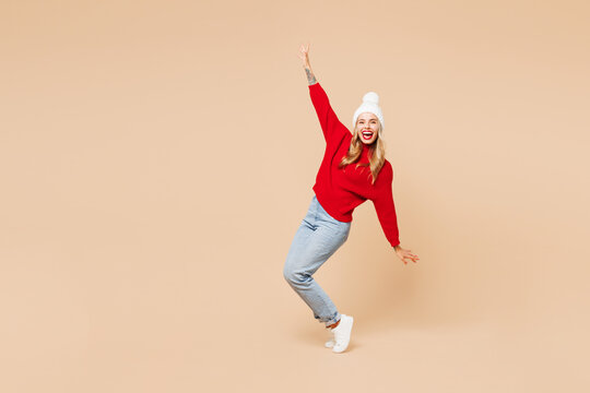 Full body merry young woman wears red sweater hat posing standing on toes lean back have fun spreading hands isolated on plain beige background. Happy New Year celebration Christmas holiday concept. - Powered by Adobe