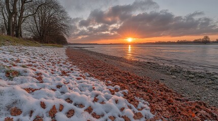 A serene riverside view at sunset, featuring snow and autumn leaves along the shore.