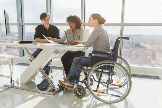 Teamwork brainstorm. Diverse multiracial colleagues woman in chair for people with disability working together. Group of people sitting in creative office discussing business. Young professional team