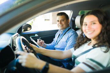 Teen girl learning to drive with a driving instructor taking notes during a driving lesson