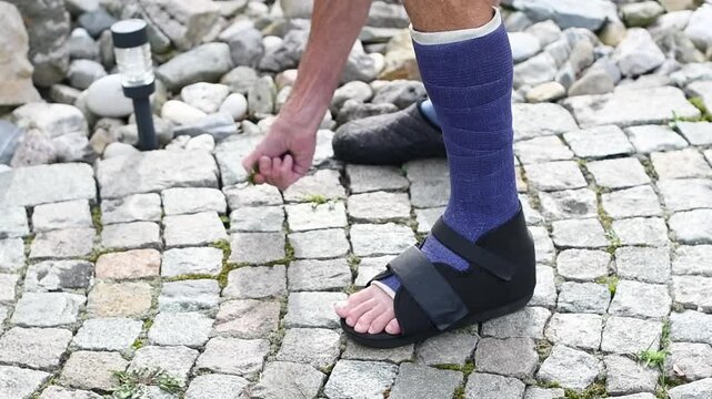 man with broken leg in purple fiberglass, weeding garden stone path, he has special sandals on his foot for walking, active lifestyle concept,
