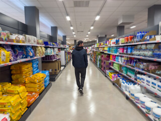 man walking between grocery shelves looking at the shelves in a supermarket