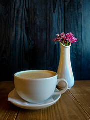 A vase with flower and a mug of coffee on the wooden table with dark wooden wall