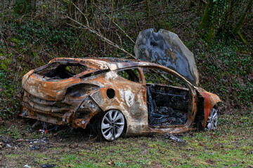 Une carcasse de voiture entièrement brulée et rouillée est stationnée sur le bord d'une route...