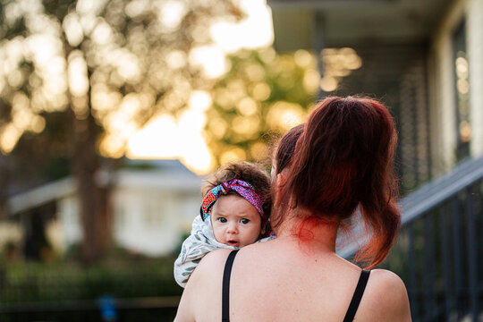 Newborn aboriginal girl peeping over mothers shoulder outside home