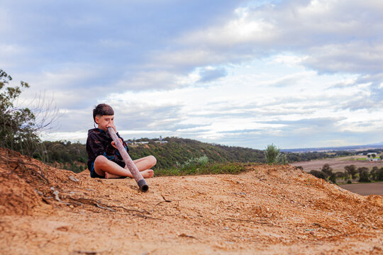 Australian cliffside landscape with aboriginal kid playing didgeridoo