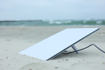 A Satellite Dish rests on the sandy beach under cloudy skies, blending nature and technology