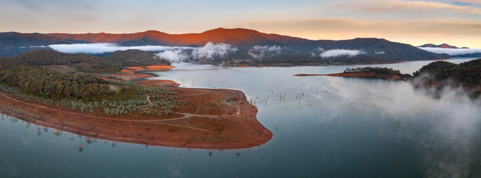 Aerial panorama of early morning light on clouds of fog and hills surrounding a high country lake