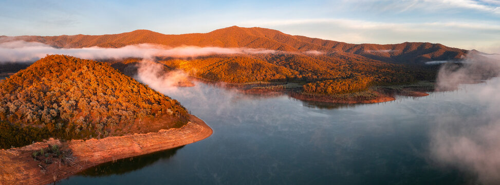 Aerial panorama of early morning light on clouds of fog and hills surrounding a high country lake
