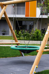 Wooden swing with a round knitted chain seat on the playground © Literat