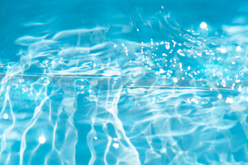 Blue water with ripples on the surface. Defocus blurred transparent blue colored clear calm water surface texture with splashes and bubbles. Water waves with shining pattern texture background.