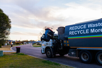 Bin truck emptying suburban rubbish bins in low light