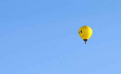 A bright yellow hot air balloon adorned with a smiley face gracefully floats against a clear blue sky, conveying a sense of joy and lightheartedness.