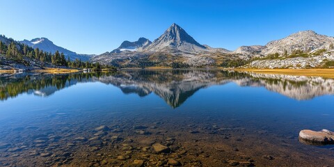 Stunning mountain landscape reflected in serene, clear lake under a bright blue sky.