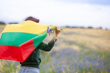 Woman holding flag of Lithuania in a rye field with blue cornflowers. Back view. Lithuanian Flag...