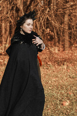 Young woman in medieval dress and cloak standing by tree in forest. Middle Ages