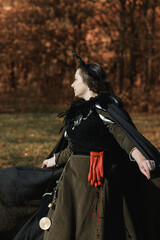 Young woman in medieval dress and cloak standing by tree in forest. Middle Ages