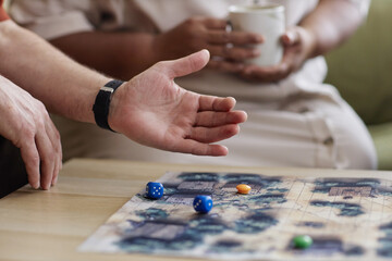 Side view closeup of senior man playing board game with focus on hand throwing dice on table copy space