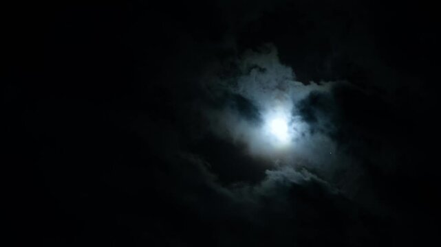 Moon and clouds in the night black sky. Clouds floating in wind blowing against the backdrop of bright moon light. Fantasy gothic scene Nighttime Time lapse. Beautiful moonlight video shot stormy sky