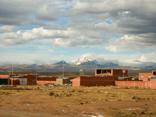 Brick-Built Houses Overlooking the Snow-Capped Mountains, the Dry Yellow Soil in the Bolivian Altiplano with a Cloudy Sky