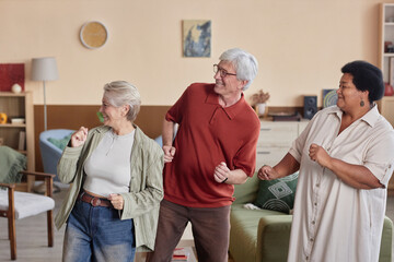 Obraz premium Group of joyful senior people dancing together enjoying disco in retirement home in muted neutral colors