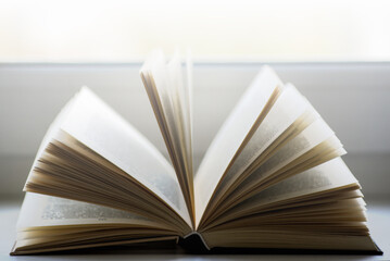 Open book on a window sill, illuminated by sunlight.