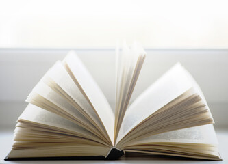Open book on a window sill, illuminated by sunlight.