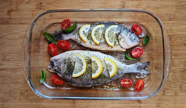 Fresh dorado fish prepared with lemon slices, cherry tomatoes, and herbs, ready for baking in dish