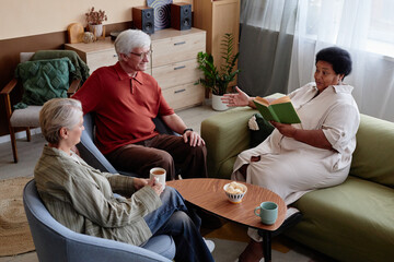High angle view at group of senior people enjoying book club discussion in cozy living room at...