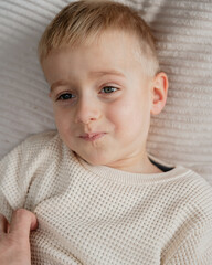 The face of a child wearing a beige sweater at home, captured in a candid moment as they try to...