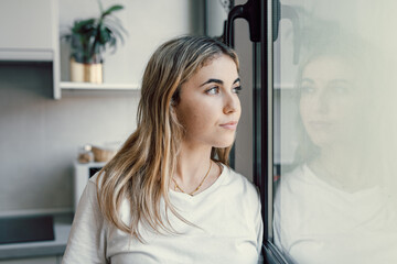 Unhappy thoughts. Worried young caucasian woman look at window feel lonely sad wait for boyfriend...
