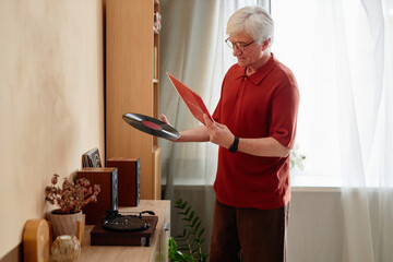 Side view portrait of white haired senior man holding vinyl records and choosing quiet home...