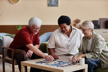 Group of elegant senior people playing board game together enjoying quiet entertainment indoors in...