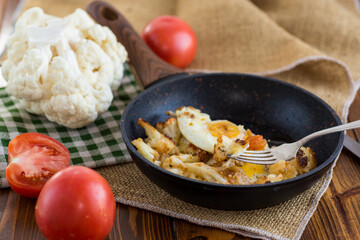 fried omelette with cauliflower and vegetables in a frying pan on a wooden table