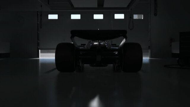 Silhouette of a race car in a dimly lit garage, garage door opens