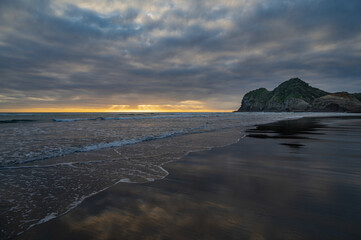 Beautiful sunset moment at the reflective Bethells surf beach, Auckland, New Zealand