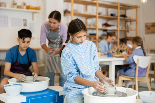 Pleased underage attendees of pottery circle working at throwing-wheel with female instructor