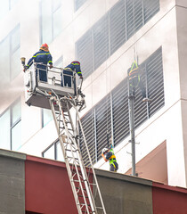 Firefighters during a rescue operation. A fire engine spraying water with a high ladder and a fire hose onto the smoke-filled roof of a burning building. firefighters on the stairs extinguish the fire