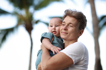 Grandmother Holding Baby Grandson  While Standing and Relaxing on Beach