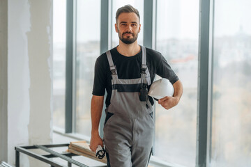 In grey uniform and black shirt. A man is renovating an unfinished room