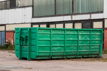 Green trash container standsnear concrete wall