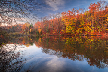 Autumn colorful foliage over lake with beautiful woods in red and yellow color. Bakony Forest and Mountain, Pisztrangos Lake, Hungary. Long exposure shot.