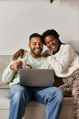 A joyful couple enjoys quality time together on a couch while using a laptop, staying warm.