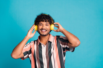 Photo of attractive funny guy wear striped shirt headphones enjoy music emtpy space isolated blue...