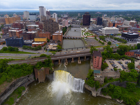 A stunning stock photo capturing the dynamic skyline of Rochester, NY, with the majestic High Falls in the foreground. The image showcases the harmonious blend of natural beauty & urban architecture.