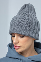 Portrait beautiful woman in grey hat. Pretty girl in warm clothes on grey background. Studio photography. Vertical photo.