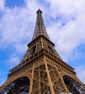 This captivating stock photo captures the Eiffel Tower in Paris, France, from a low-angle perspective looking up. The iconic structure stands tall against a vibrant blue sky filled with white clouds.