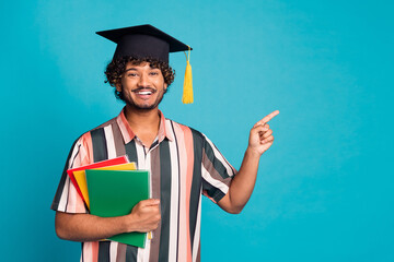 Photo of attractive funny guy wear striped shirt mortarboard finish education pointing emtpy space...