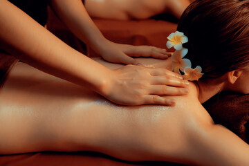 Caucasian couple customer enjoying relaxing anti-stress spa massage and pampering with beauty skin recreation leisure in warm candle lighting ambient salon spa at luxury resort or hotel. Quiescent